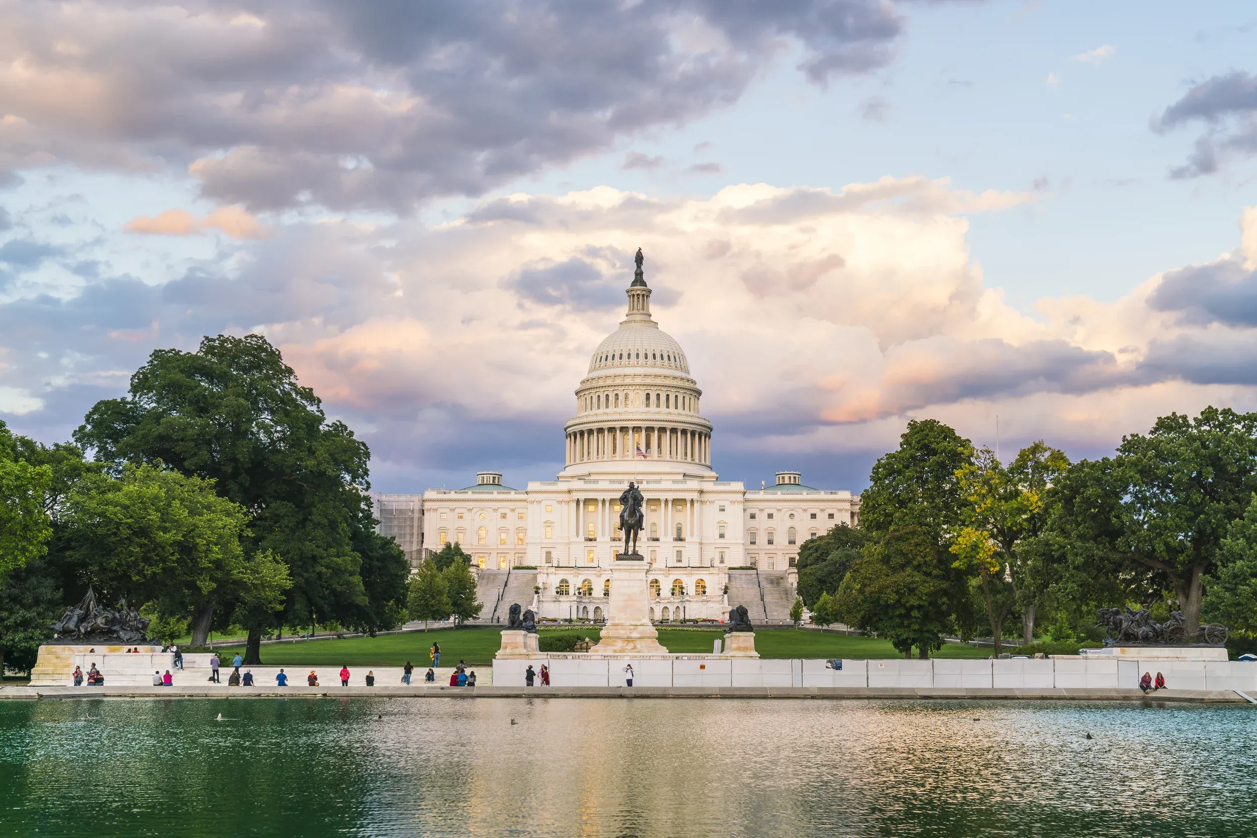 united states congress building front in daytime with clouds in the sky and large pond in the foreground reflecting the scenery