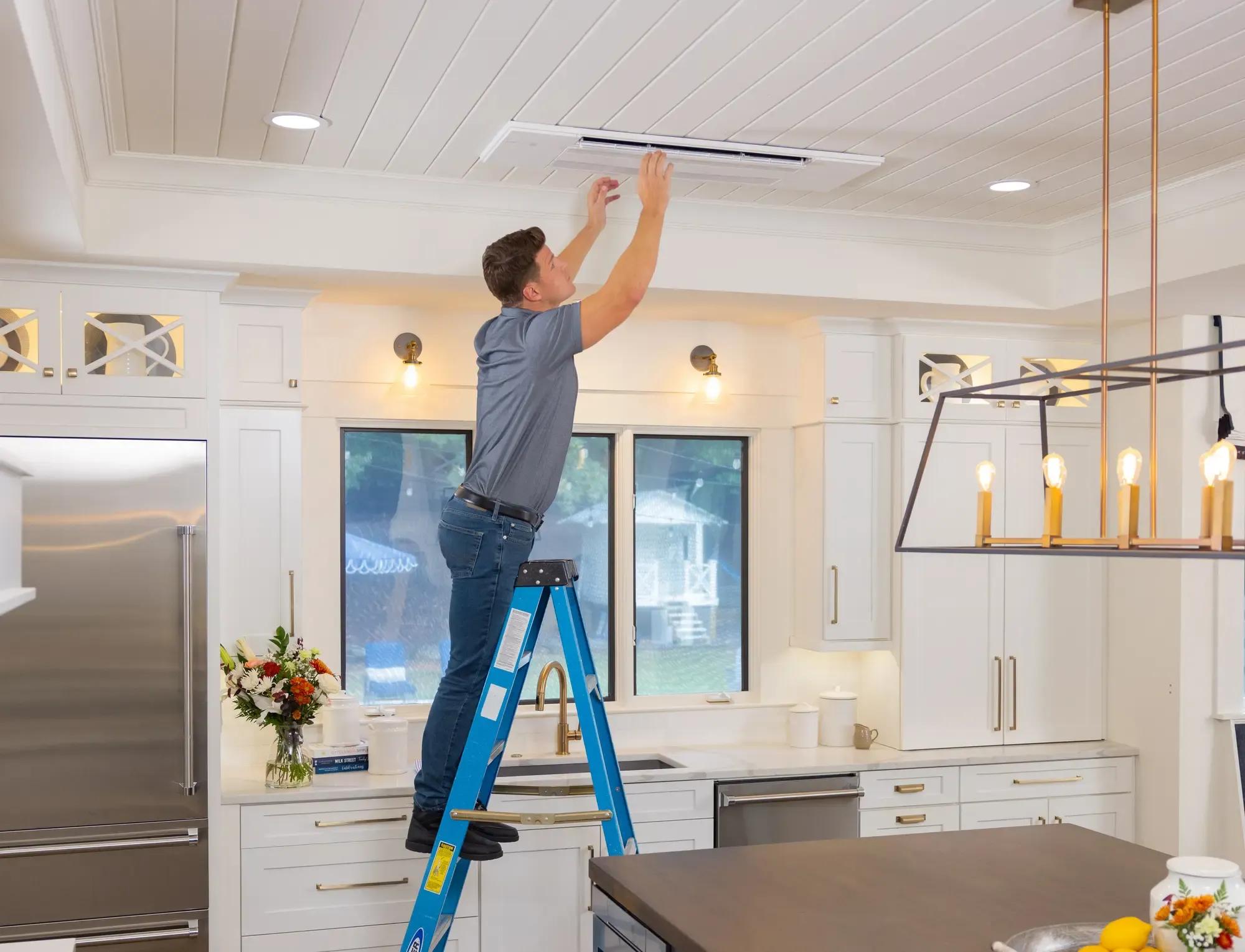 contractor on a ladder installing a ceiling cassette unit in a modern kitchen