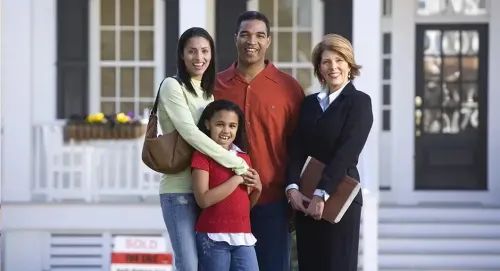 young family smiling in front of house with real estate agent