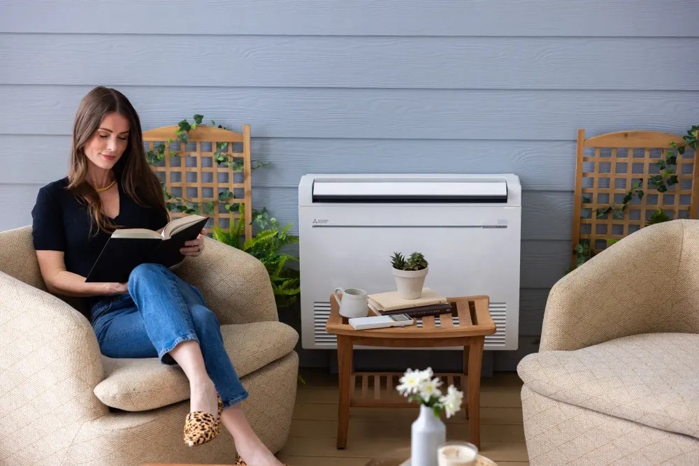 young woman sitting and reading with mitsubishi electric low-wall-mounted indoor unit to her right