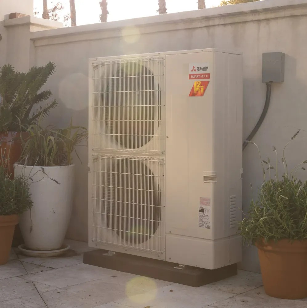 Mitsubishi Electric outdoor heat pump unit on patio with plants and artistic lense flare