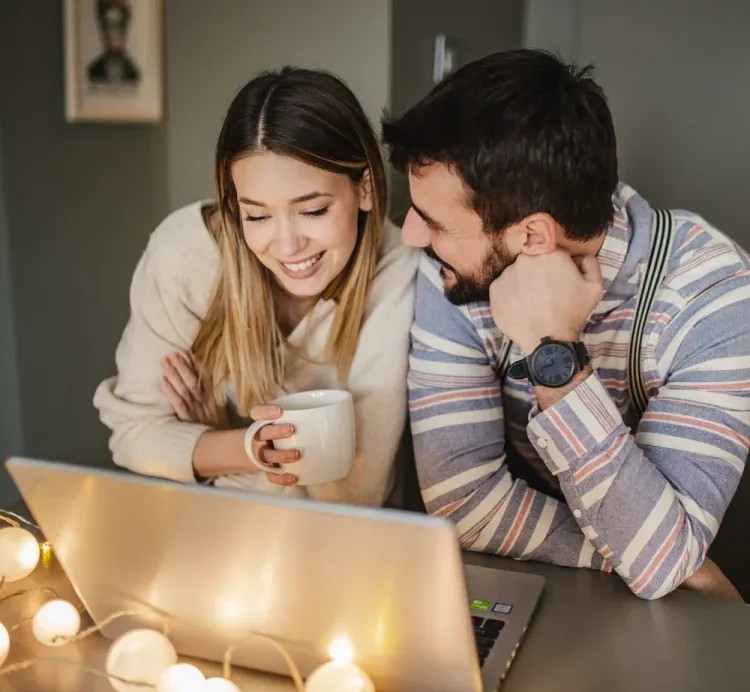 young smiling couple looking at laptop in winter wearing sweaters